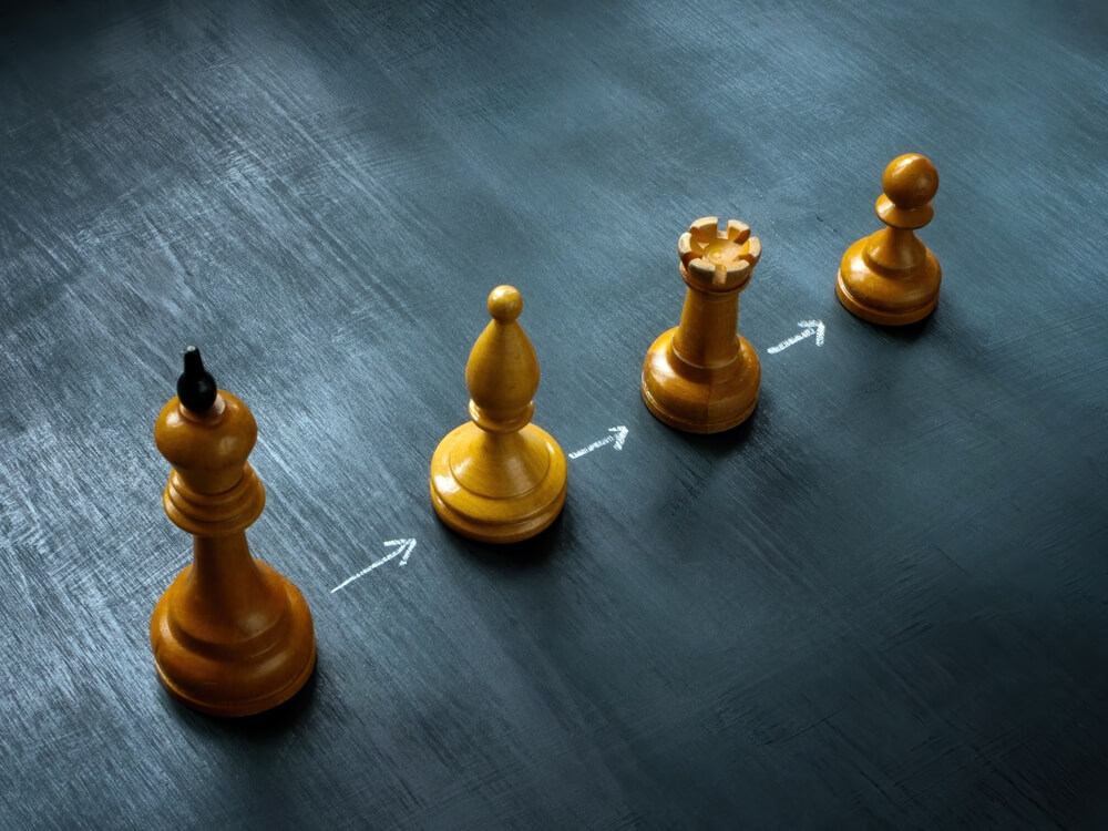 Four wooden chess pieces—king, bishop, rook, and pawn—are strategically lined up on a textured dark surface. White arrows point from left to right, creating an efficient sequence reminiscent of public sector organization. Subtle lighting casts shadows that highlight the pieces' intricate details.
